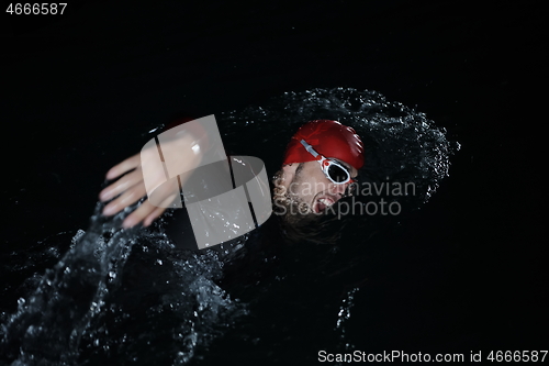 Image of triathlon athlete swimming in dark night wearing wetsuit