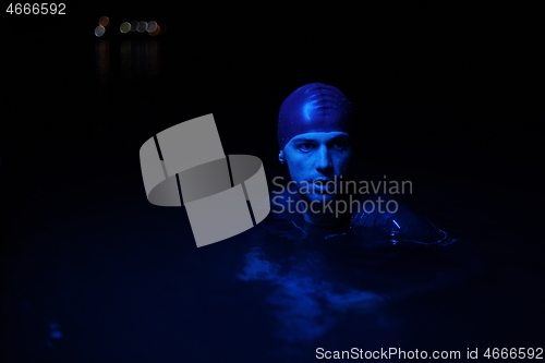 Image of authentic triathlete swimmer having a break during hard training on night neon gel light