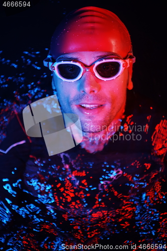 Image of authentic triathlete swimmer having a break during hard training on night neon gel light