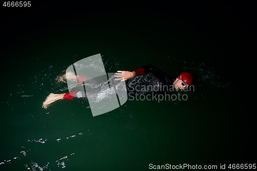 Image of triathlon athlete swimming in dark night wearing wetsuit