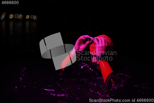 Image of authentic triathlete swimmer having a break during hard training on night neon gel light