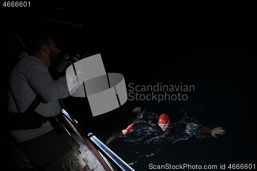 Image of videographer taking action shot of triathlon swimming athlete at night