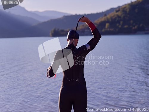 Image of authentic triathlon athlete getting ready for swimming training on lake