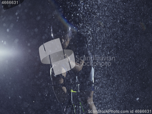 Image of triathlon athlete riding bike on rainy night