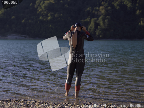 Image of authentic triathlon athlete getting ready for swimming training on lake