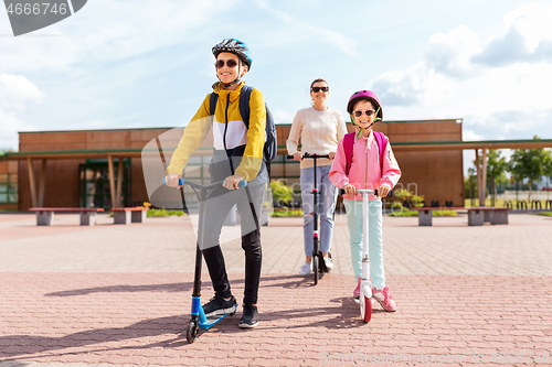 Image of happy school children with mother riding scooters