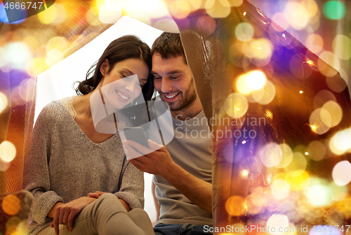 Image of happy couple with smartphone in kids tent at home