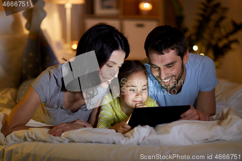 Image of family with tablet pc in bed at night at home