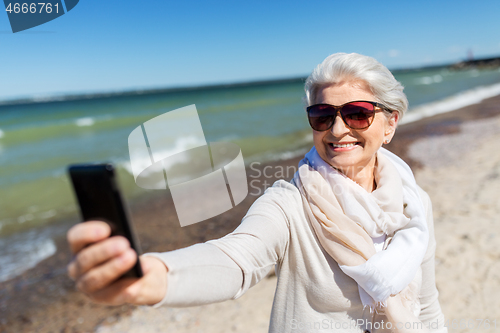Image of senior woman taking selfie by smartphone on beach