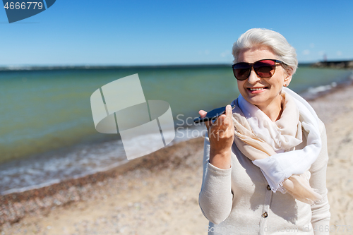 Image of old woman recording voice by smartphone on beach