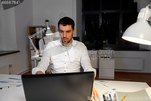 Image of businessman with laptop working at night office