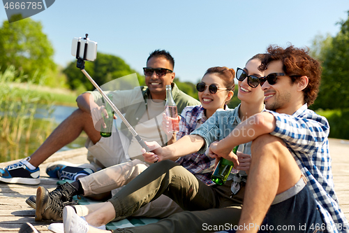 Image of friends with drinks taking selfie on lake pier