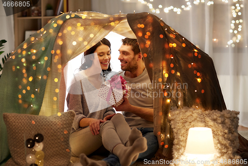 Image of happy couple with gift box in kids tent at home