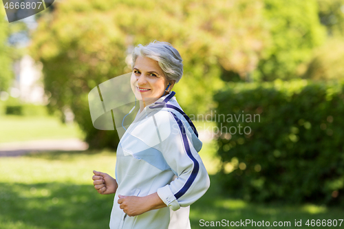 Image of senior woman with earphones running in summer park