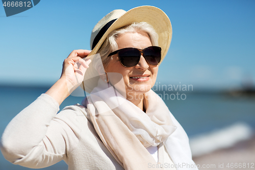 Image of happy senior woman in sunglasses and hat on beach