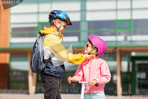 Image of school boy fastening girl\'s helmet for scooter