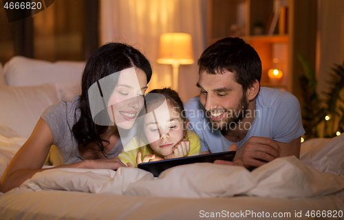 Image of family with tablet pc in bed at night at home