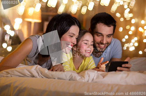 Image of happy family with smartphone in bed at night