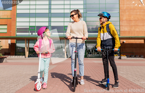 Image of happy school children with mother riding scooters