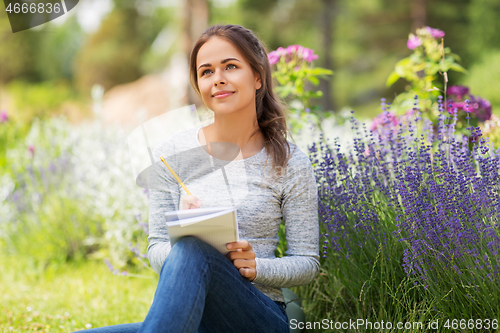 Image of young woman writing to notebook at summer garden