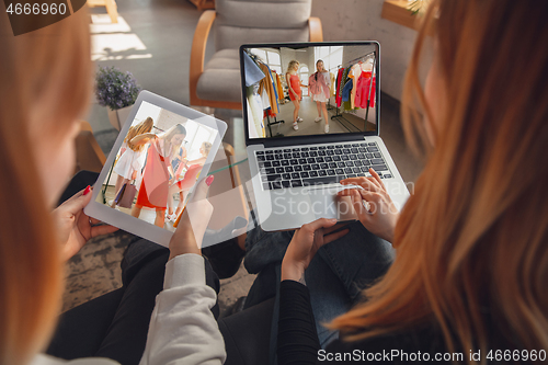 Image of Two friends watching online shopping, TV or cinema together with devices