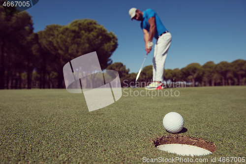 Image of golf player hitting shot, ball on edge of hole