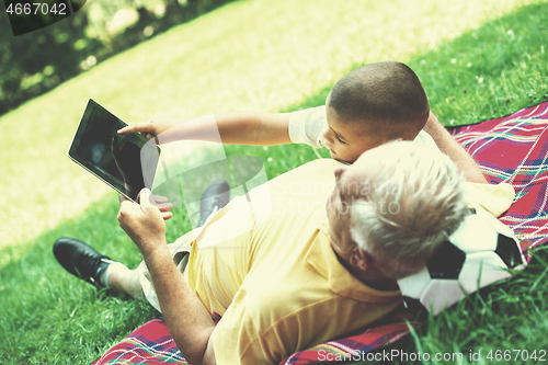 Image of grandfather and child in park using tablet