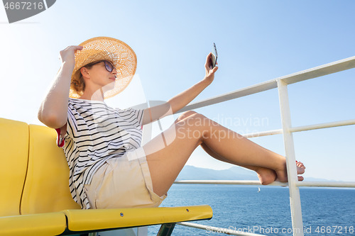 Image of Beautiful, romantic blonde woman taking selfie self portrait photo on summer vacations traveling by cruse ship ferry boat.