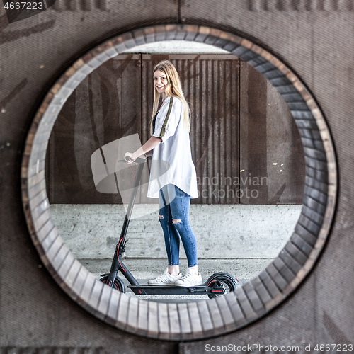 Image of Casual caucasian teenager riding urban electric scooter in urban environment. Urban mobility concept