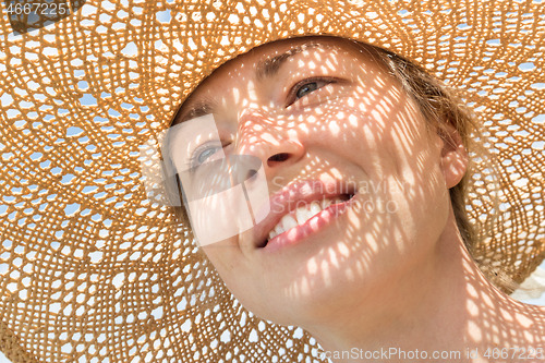 Image of Close-up portrait of woman wearing straw hat enjoying summer sun. Pattern of shadows falling on her face