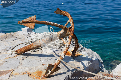 Image of Old rusty anchor on rock by blue sea