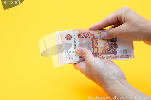 Image of Two hands holding a crustacean of five thousandth Russian rubles on a yellow background