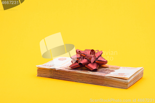 Image of On the bundle of five thousandth bills lies a red bow, yellow background