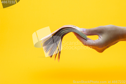 Image of Hand holds out a wad of money, yellow background