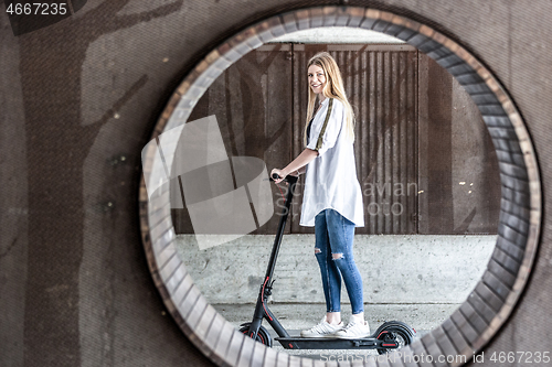 Image of Casual caucasian teenager riding urban electric scooter in urban environment. Urban mobility concept