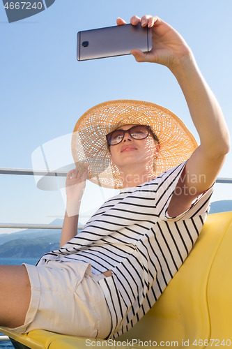 Image of Beautiful, romantic blonde woman taking selfie self portrait photo on summer vacations traveling by cruse ship ferry boat.