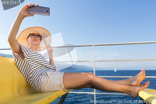 Image of Beautiful, romantic blonde woman taking selfie self portrait photo on summer vacations traveling by cruse ship ferry boat.