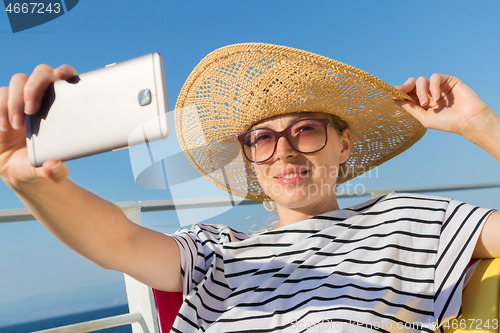 Image of Beautiful, romantic blonde woman taking selfie self portrait photo on summer vacations traveling by cruse ship ferry boat.