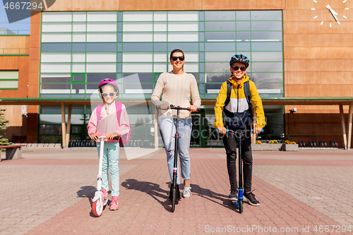 Image of happy school children with mother riding scooters