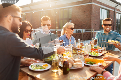 Image of happy friends eating at barbecue party on rooftop