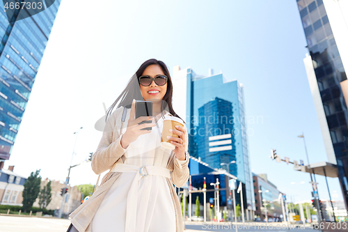 Image of smiling woman with smartphone and coffee in city