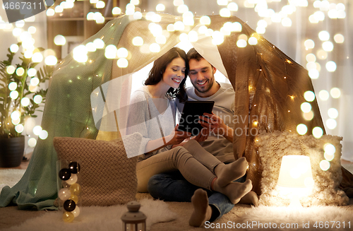 Image of happy couple with tablet pc in kids tent at home