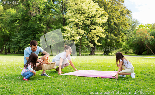 Image of family laying down picnic blanket in summer park