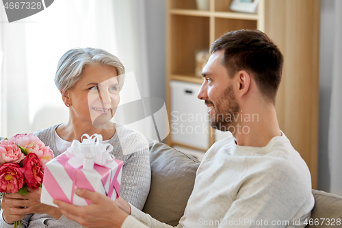 Image of son giving present and flowers to senior mother