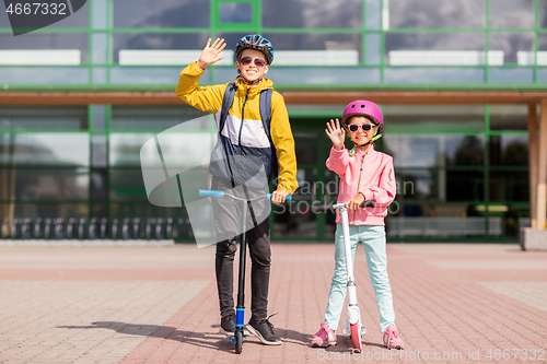 Image of happy school children in helmets riding scooters