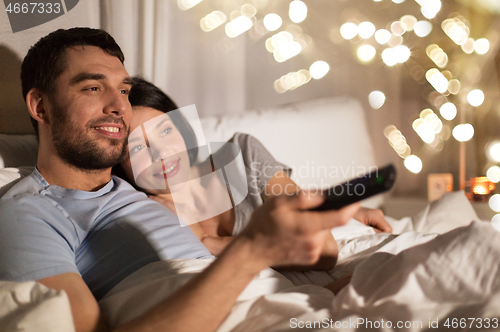 Image of happy couple watching tv in bed at night at home