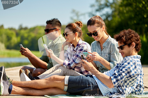 Image of friends with smartphone on lake pier in summer