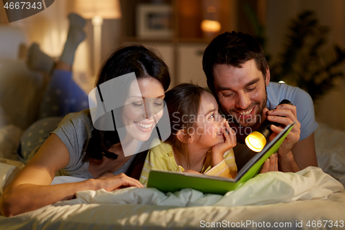 Image of happy family reading book in bed at night at home