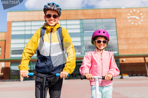 Image of happy school children in helmets riding scooters