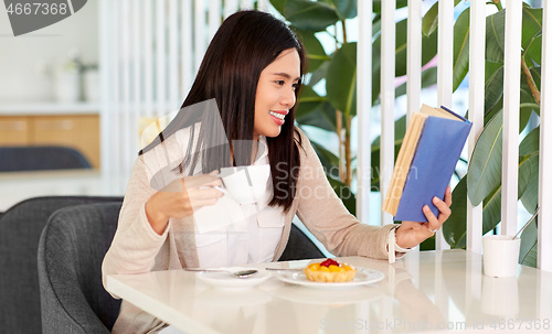 Image of woman drinking coffee and reading book at cafe